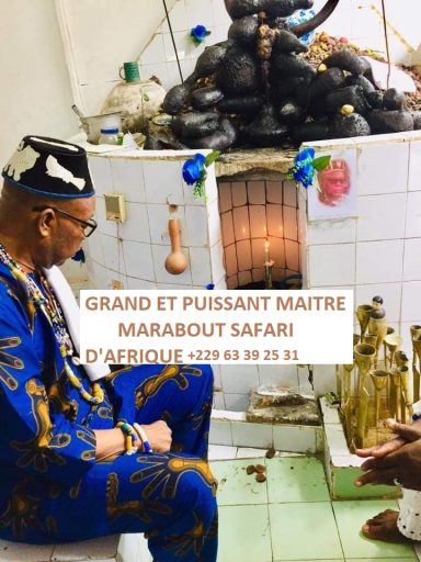 Homme en tenue traditionnelle assis devant des statues et un autel, avec des inscriptions.